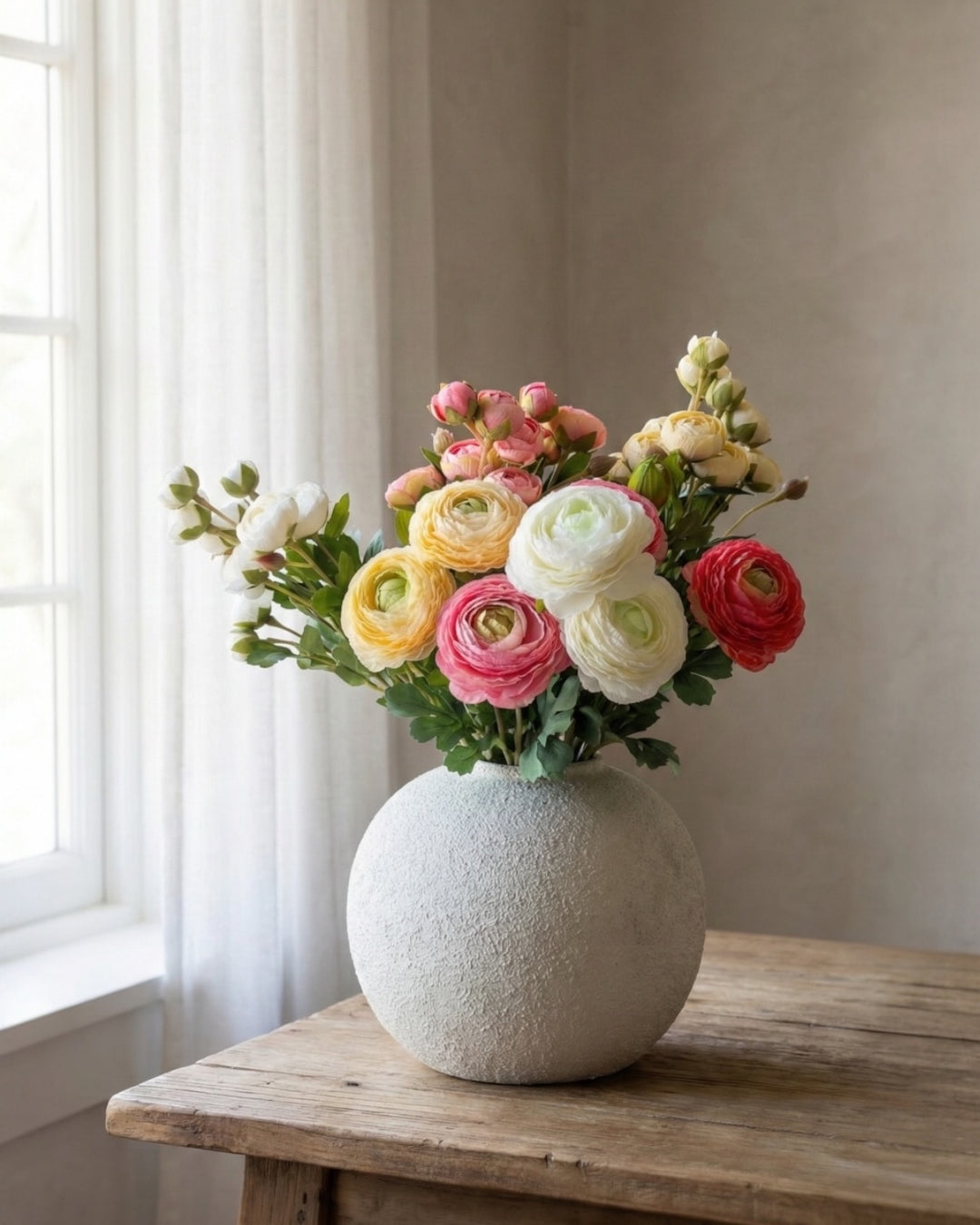 Warm-toned ranunculus faux flowers and greenery stems perfectly arranged in a white round vase, highlighting allergy-friendly and wilt-proof floral design
