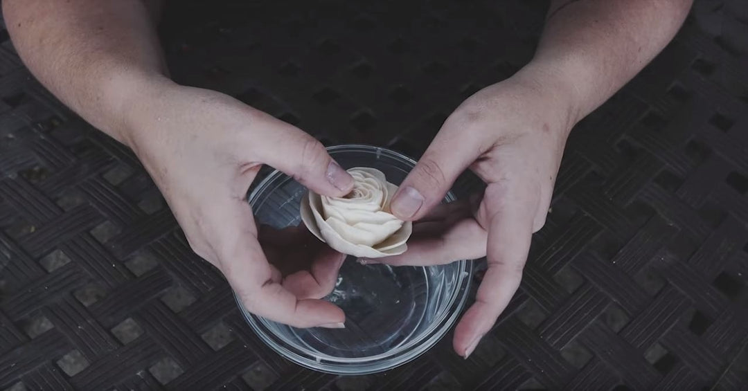 Hands carefully reshaping the petals of a raw cream sola wood flower over a clear glass bowl.