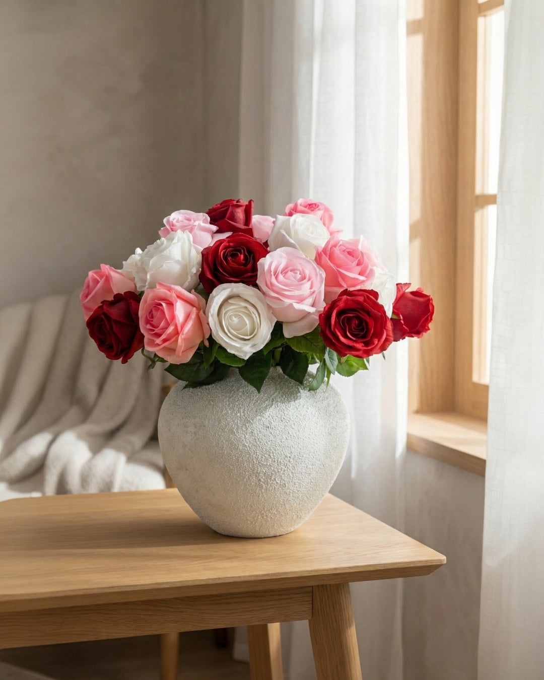 A lush arrangement of red, pink, and white faux roses styled in a round textured white ceramic vase on a wooden table, representing maintenance-free home decor from Luv Sola Flowers