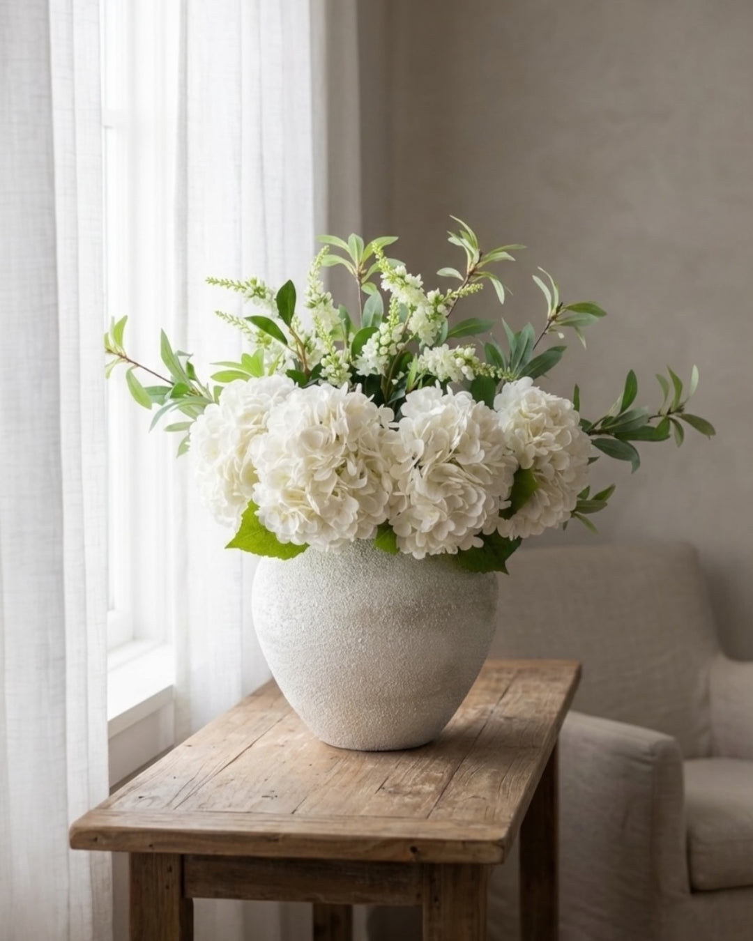 Professional styling of white real-touch hydrangeas and green faux filler stems in a white ceramic vase, showcasing realistic leaf veining and botanical detail